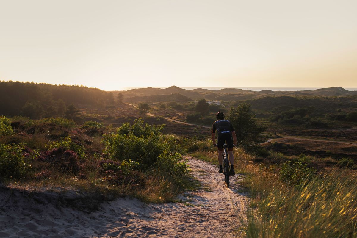 Mountainbiker die door een duinpad fietst met ondergaande zon